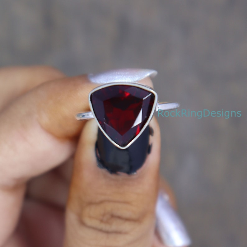 Puede incluir: Un anillo de plata con una piedra preciosa roja triangular. El anillo est&aacute; en un dedo.