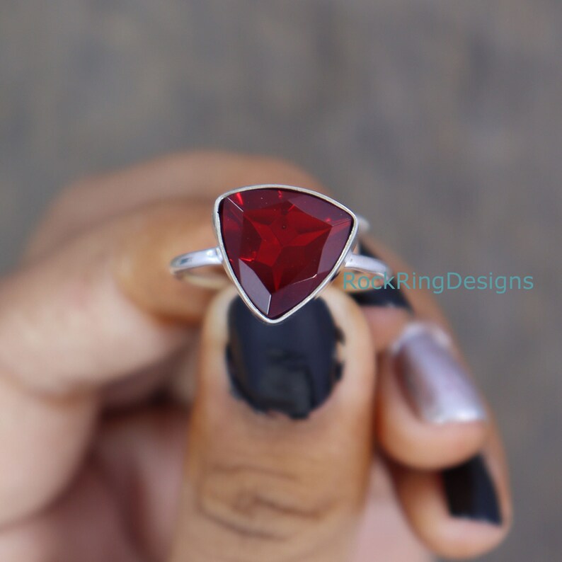 Puede incluir: Un anillo de plata con una piedra preciosa roja triangular. El anillo est&aacute; engastado en una banda simple y la piedra preciosa est&aacute; facetada.