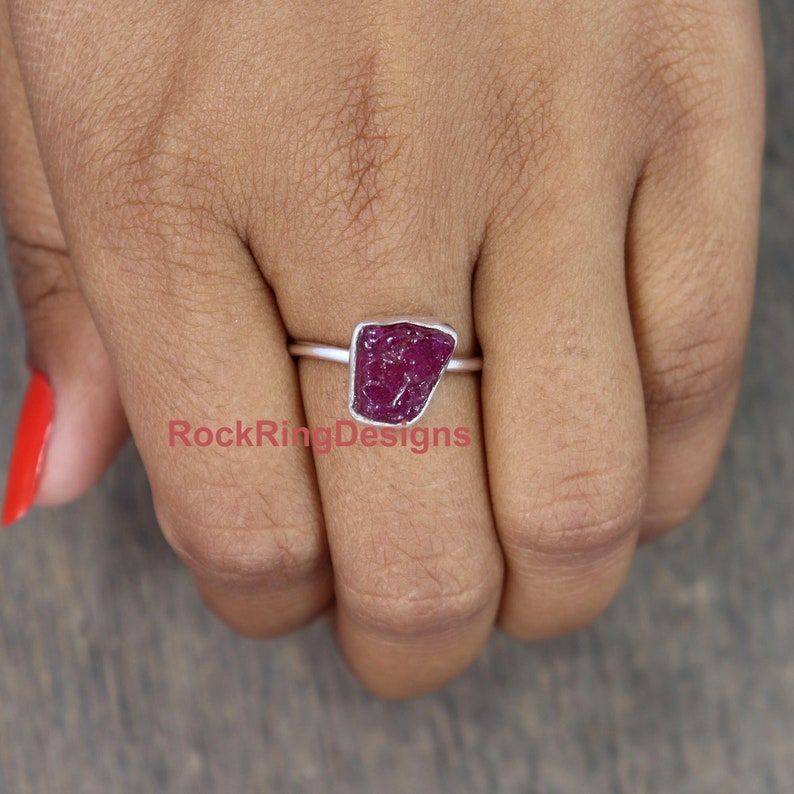K&ouml;nnte beinhalten: Ein Silberring mit einem rohen, roten Rubin-Edelstein. Der Ring ist auf einem schlichten Silberband gefasst.