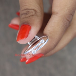 K&ouml;nnte beinhalten: Ein silberner Ring mit zwei B&auml;ndern und kleinen runden Akzenten. Der Ring befindet sich an einem Finger mit rotem Nagellack.