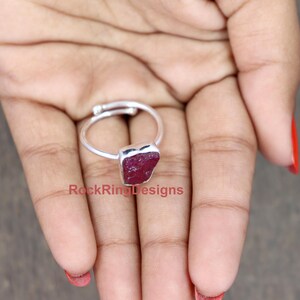 K&ouml;nnte beinhalten: Ein silberner Ring mit einem gro&szlig;en, rohen, roten Rubin-Edelstein. Der Ring wird an einem Finger getragen. Unter dem Ring steht 'RockRingDesigns'.