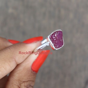 K&ouml;nnte beinhalten: Ein Silberring mit einem rohen, rosafarbenen Rubin-Edelstein. Der Ring hat eine einfache Band und der Rubin ist in einer nat&uuml;rlichen, rohen Form.