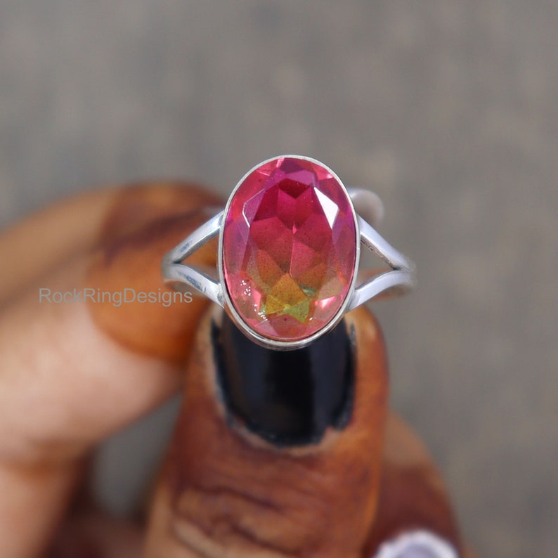 May include: A silver ring with a large oval-shaped gemstone. The gemstone is a deep red color with a green and yellow iridescent sheen.