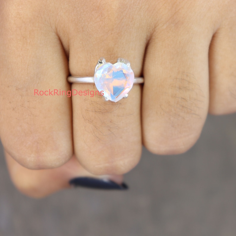Pu&ograve; includere: Un anello d'argento con una pietra di opale a forma di cuore. L'opale &egrave; iridescente e ha una tonalit&agrave; rosa.