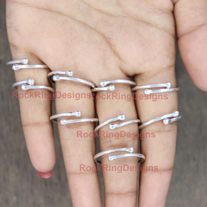 K&ouml;nnte beinhalten: Ein Satz verstellbarer Silberringe mit einer kleinen Kugel an jedem Ende. Die Ringe sind auf den Fingern einer Person gestapelt.