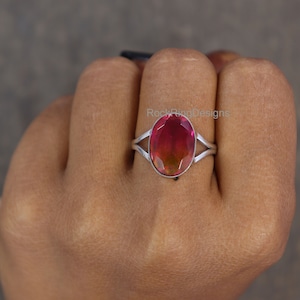 May include: A silver ring with a pink and green oval gemstone. The ring is set with a simple band and has a split shank. The text "Rock Ring Designs" is visible in the background.