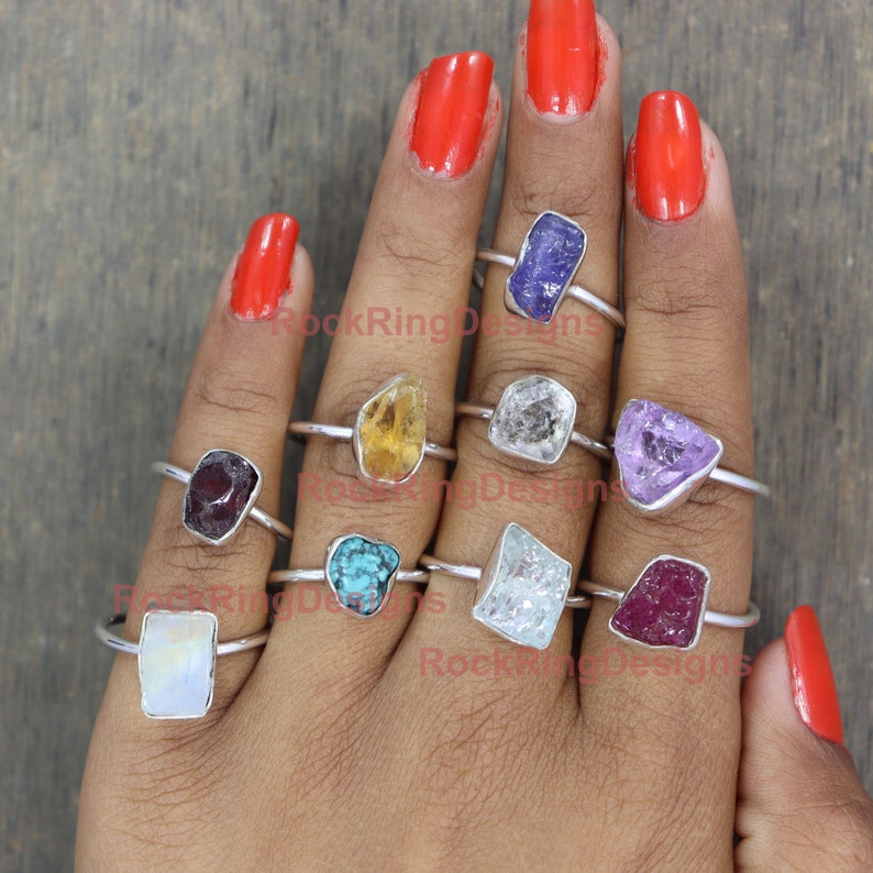 K&ouml;nnte beinhalten: Eine Hand tr&auml;gt neun Silberringe mit verschiedenen farbigen Edelsteinen. Die Edelsteine umfassen Amethyst, T&uuml;rkis, Rubin, Citrin, Mondstein, Aquamarin und klaren Quarz.