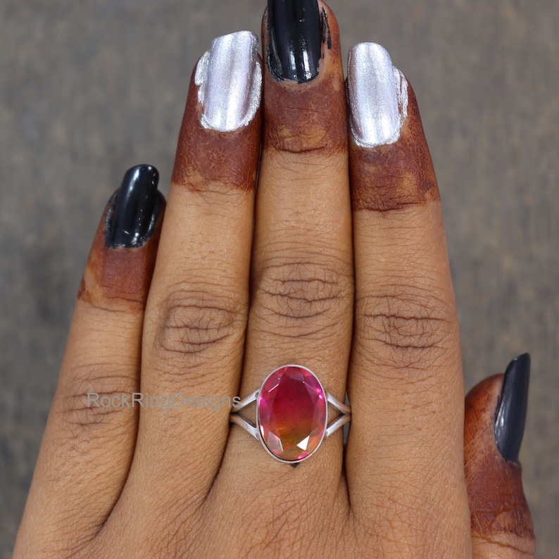May include: A silver ring with a large oval-shaped pink and orange gemstone. The ring is on a person's finger.