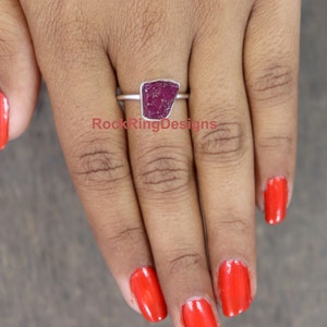 K&ouml;nnte beinhalten: Ein Silberring mit einem gro&szlig;en, rohen, tiefrot gef&auml;rbten Rubinstein. Der Ring wird an einem Finger getragen.