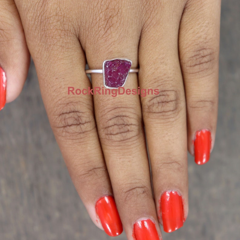 K&ouml;nnte beinhalten: Ein Silberring mit einem gro&szlig;en, rohen, tiefrot gef&auml;rbten Rubinstein. Der Ring wird an einem Finger getragen.