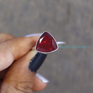 Puede incluir: Un anillo de plata con una piedra roja triangular. El anillo est&aacute; engastado en una banda simple.