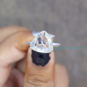 Puede incluir: Un anillo de plata con una piedra preciosa triangular transparente. El anillo est&aacute; en un dedo.