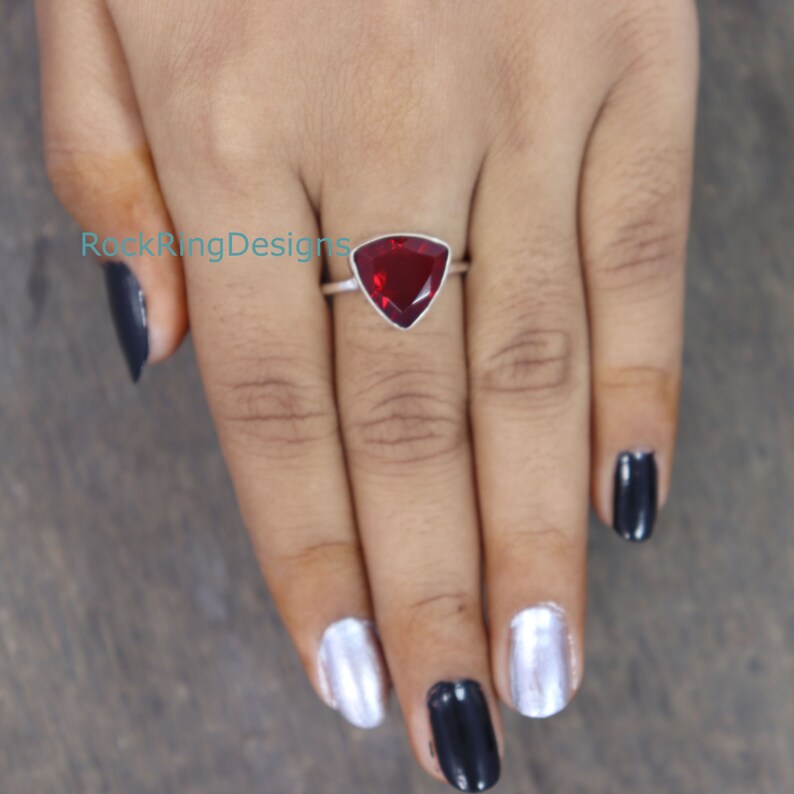 Puede incluir: Un anillo de plata con una piedra roja triangular. El anillo est&aacute; en el dedo de una persona.