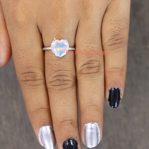 Pu&ograve; includere: Un anello d'argento con una grande pietra preziosa a forma di cuore iridescente.