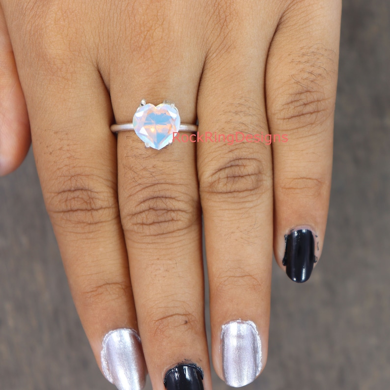 Pu&ograve; includere: Un anello d'argento con una grande pietra preziosa a forma di cuore iridescente.