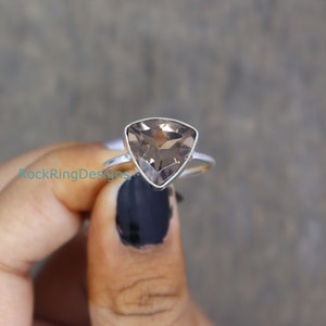 Puede incluir: Un anillo de plata con una piedra preciosa de cuarzo ahumado triangular. El anillo est&aacute; en un dedo con esmalte de u&ntilde;as negro.