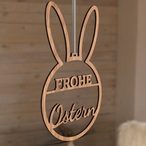 Może przedstawiać: Drewniana ozdoba wielkanocna w kształcie kr&oacute;lika z napisem "Frohe Ostern" w k&oacute;łku.