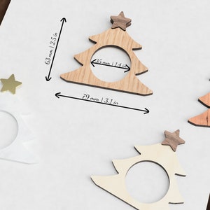 May include: Three wooden Christmas tree napkin rings with gold stars on top. The rings are 3.1 inches wide and 2.5 inches tall.