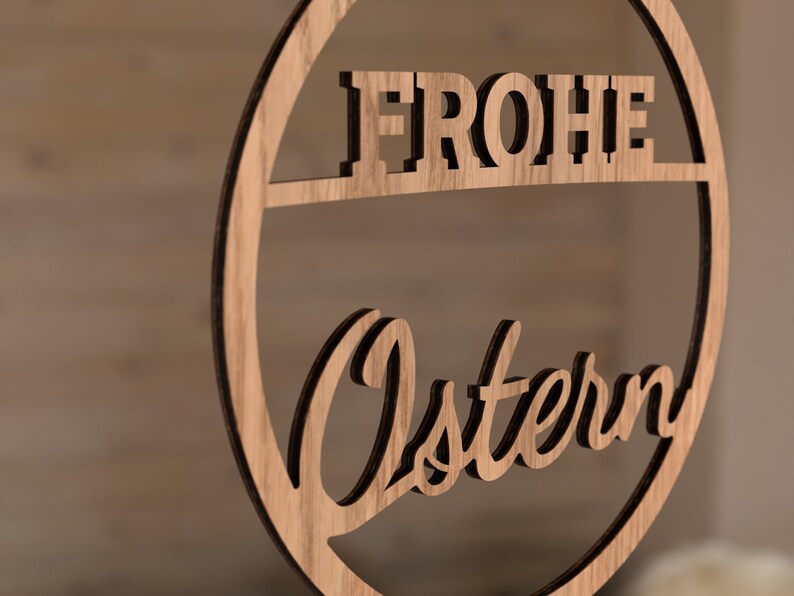 Może przedstawiać: Drewniane koło z wyciętymi słowami "Frohe Ostern" w ozdobnym kroju pisma. Koło jest jasnobrązowe i ma naturalne usłojenie drewna.