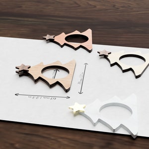 May include: Four wooden Christmas tree napkin rings in different shades of brown and white. The rings are 6.9 cm (2.7 inches) wide and 7.2 cm (2.8 inches) tall.