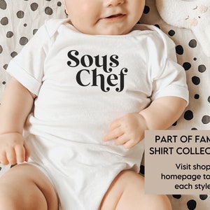 May include: White baby bodysuit with the words "Sous Chef" in black script. The bodysuit is short-sleeved. The image also includes a beige rectangle with the text "PART OF FAMILY SHIRT COLLECTION" and a call to action to visit the shop.
