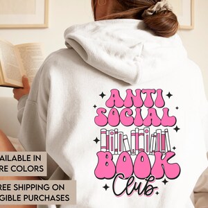 Può includere: Una felpa con cappuccio bianca con una grafica rosa che dice "Anti Social Book Club" con una pila di libri e stelle.