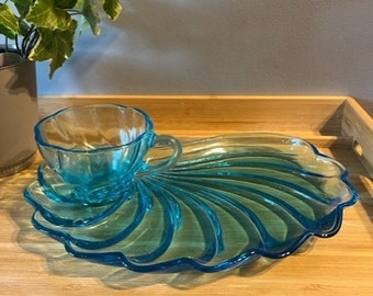 May include: A blue glass seashell-shaped serving dish with a matching blue glass cup. The dish has a scalloped edge and is perfect for serving snacks or desserts.
