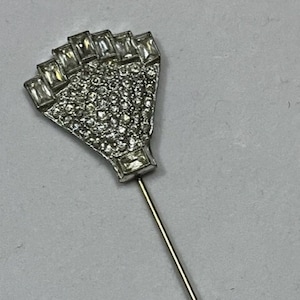 May include: A silver and gold tone brooch with a fan-shaped design. The fan is made of clear rhinestones and has a gold tone pin.