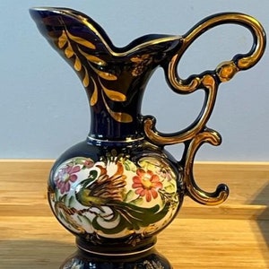 Könnte beinhalten: Eine blaue und goldene Keramikkanne mit Blumenmuster. Die Kanne hat einen breiten Boden und einen schmalen Hals mit einem gebogenen Griff.