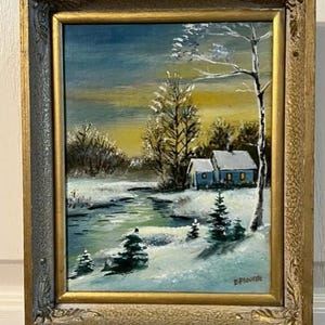 May include: A framed painting depicting a winter scene with a small blue house, snow-covered trees, and a winding stream. The painting is signed "E. Flouride" in the bottom right corner.