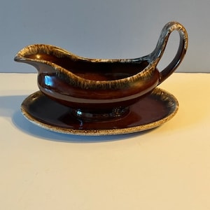 Könnte beinhalten: Eine braune und weiße glasierte Keramik-Soßenkännchen mit Henkel und einer passenden Untertasse.