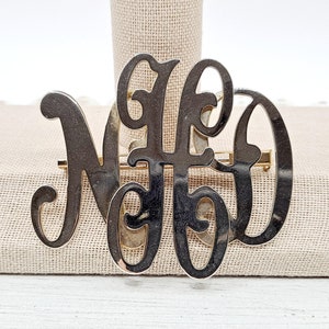 May include: A silver-toned monogram brooch with the letters "NED" in a script font.