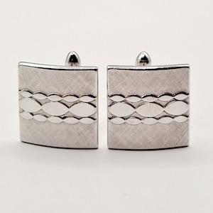 May include: A pair of silver cufflinks with a textured design featuring a row of oval shapes.