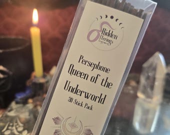 May include: A package of incense sticks with the text "Persephone Queen of the Underworld" and "30 Stick Pack." The label features a logo with a crescent moon design. A lit candle and a crystal are in the background.