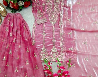 Può includere: Un completo rosa di tre pezzi composto da una tunica a maniche lunghe, una gonna plissettata e una sciarpa trasparente abbinata. La tunica e la gonna presentano ricami argentati, paillettes e piccoli dettagli di perle bianche.