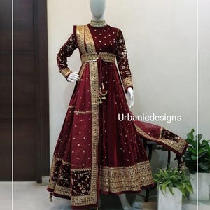 May include: A burgundy velvet gown with gold embroidery and embellishments. The long-sleeved dress features a high neckline, a fitted bodice, and a flowing skirt. The text "Urbanicdesigns" is visible on the dress.