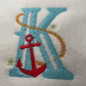 May include: Embroidered letter K in blue with white stripes, a red anchor, and a gold rope design. The letter is surrounded by small yellow stars.