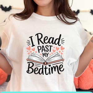 Peut inclure: T-shirt blanc avec l'inscription "I Read Past My Bedtime" en noir. Le motif comprend un livre ouvert et des cœurs roses. Le t-shirt a un col rond et des manches courtes. Le texte "PNG & SVG" et "TRENDING DESIGNS" est également visible.