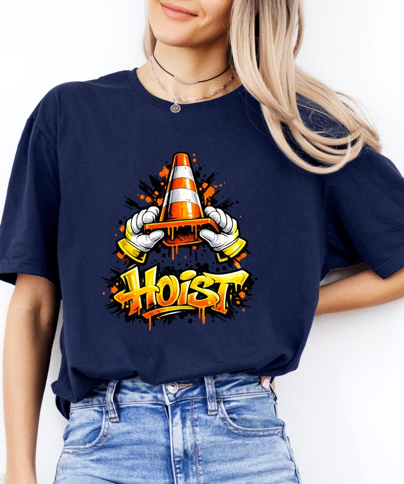 May include: Navy blue t-shirt featuring a graphic of a traffic cone held by cartoon hands with the word "Hoist" in yellow graffiti style. The design includes orange paint splatter effects.