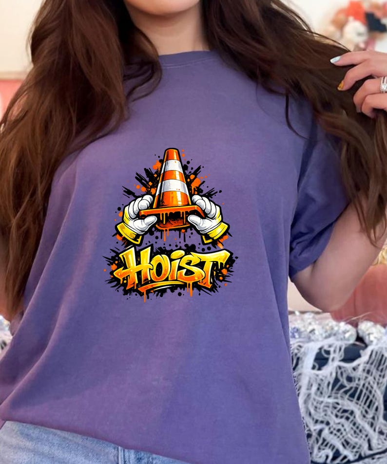 May include: A purple t-shirt featuring a graphic of a traffic cone held by gloved hands, with the word "Hoist" in graffiti-style lettering. The design includes orange and black accents.