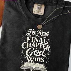 Peut inclure: Un t-shirt noir à col rond avec une impression graphique blanche représentant un livre ouvert et le texte I've Read The FINAL CHAPTER God Wins. Le t-shirt comporte une étiquette de cou beige avec le texte Comfort Colors et une étiquette S M CH.