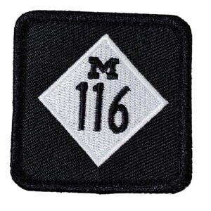 Könnte beinhalten: Ein quadratischer, schwarzer Aufnäher mit einem weißen Diamanten in der Mitte. Der Diamant enthält den Buchstaben "M" über der Zahl "116" in Schwarz. Der Aufnäher hat einen genähten Rand.