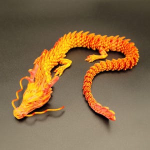 Könnte beinhalten: Eine flexible, bewegliche Drachenfigur mit einem lebendigen Farbverlauf aus gelben, orangen und roten Schuppen. Das Wesen hat einen detaillierten Kopf mit langen, fließenden Schnurrhaaren, vier bekrallte Gliedmaßen und einen langen Körper.