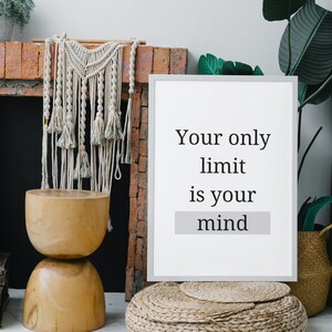 Könnte beinhalten: Ein weiß gerahmtes Motivationsposter mit dem Text "Your only limit is your mind" in schwarzer Schrift. Das Poster lehnt an einem gemauerten Kamin mit einem Makramee-Wandbehang und einem Holzhocker davor.