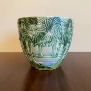 Peut inclure: Un pot en céramique vert avec un motif en relief de fleurs et d'arbres. Le pot a une finition émaillée et une forme arrondie.