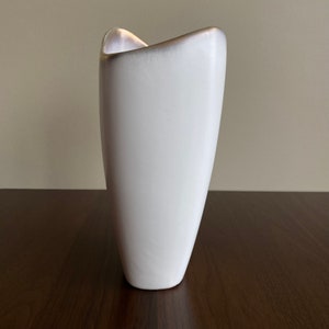 May include: A white ceramic vase with a unique, modern design. The vase has a smooth, glossy finish and a slightly curved shape.