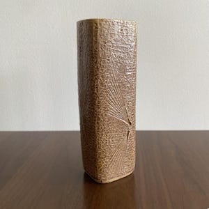 Peut inclure: Un vase rectangulaire en céramique marron avec une surface texturée et un motif en forme d'éventail. Le vase mesure environ 20 cm de haut et a une base légèrement incurvée. Le vase est posé sur une surface en bois brun foncé.