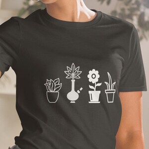 May include: A black t-shirt with a white graphic of a marijuana plant, a bong, a flower, and a potted plant. The graphic is centered on the shirt.