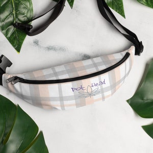 May include: A white and pink plaid fanny pack with a black adjustable strap. The fanny pack has a zipper closure and a purple logo that says "Pot Head" with a marijuana leaf.