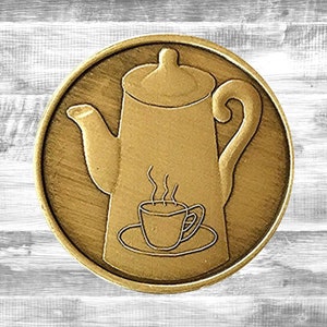 May include: A gold-colored metal coin with a design of a coffee pot and a steaming cup of coffee on a saucer.
